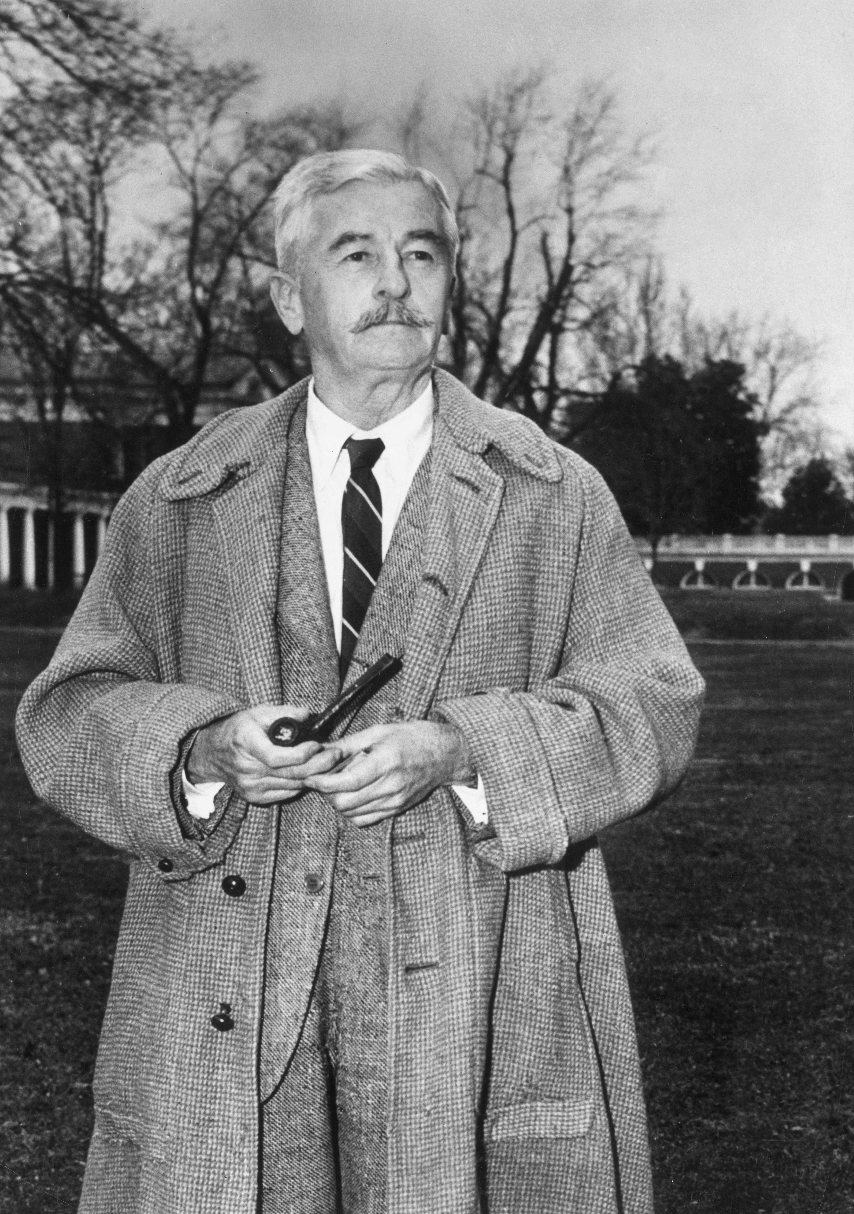 circa 1960: American author William Faulkner (1897 - 1962) stands outdoors, wearing a tweed overcoat and holding a pipe. (Photo by Hulton Archive/Getty Images)
